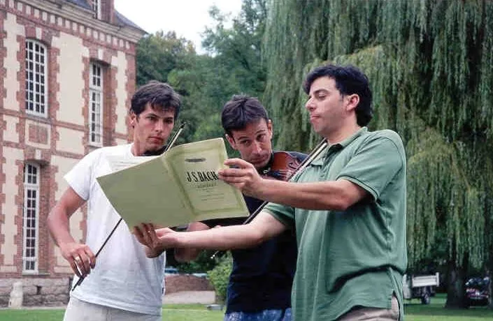 Danny, violin in hand, reading a Bach score with two friends